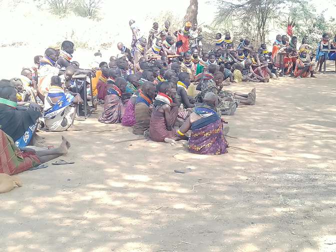 Community members seated in the shade at an outdoor meeting
